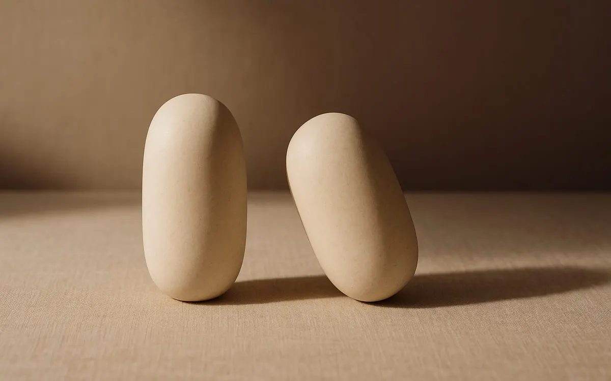Two matching pale stone forms on warm linen, one upright and one leaning, a still life standing in for facial symmetry and imbalance