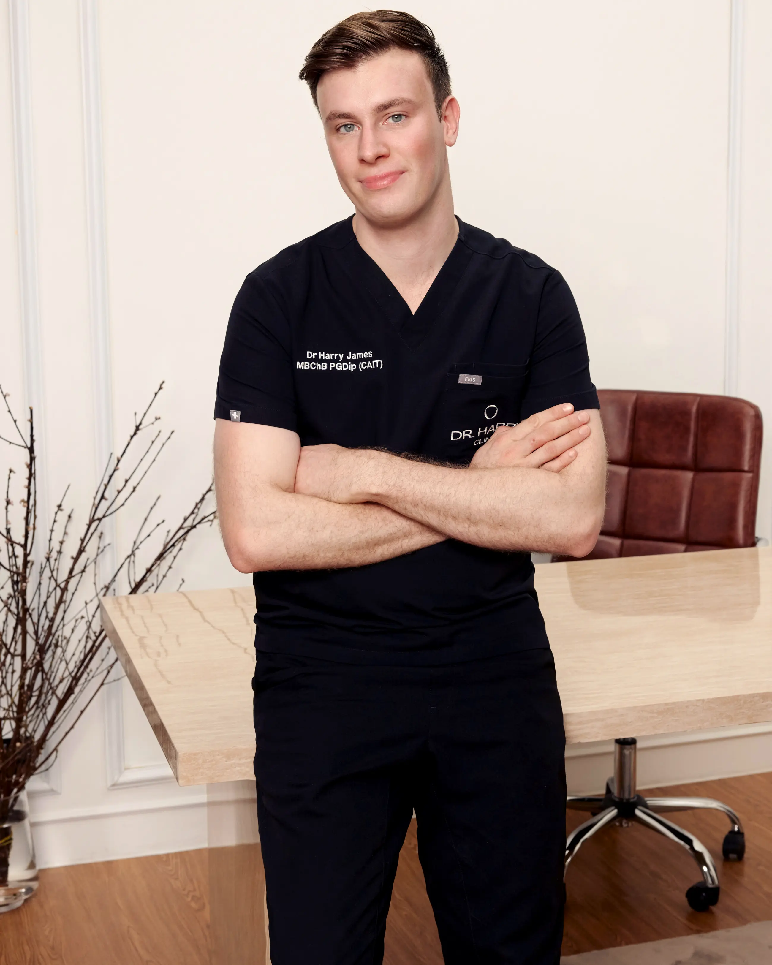 Dr Harry James standing with arms folded beside the consultation desk at Dr Harry Clinic